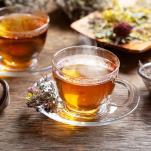 Cups of herbal tea with various herbs on wooden table