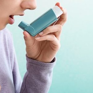 Young woman using inhaler against asthma on color background